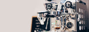 A Rocket Espresso Appartamento espress machine next to a sandwhich board, against an all white background