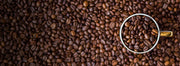 Topdown look at a cup filled with whole bean coffee and espresso, surrounded by coffee beans.