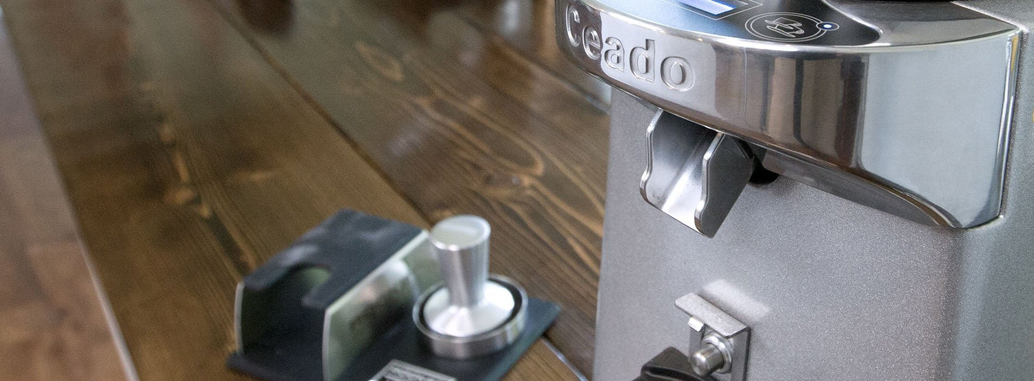 Closeup of the dispensing chute of a Ceado coffee grinder, which sits on a finished wooden table.
