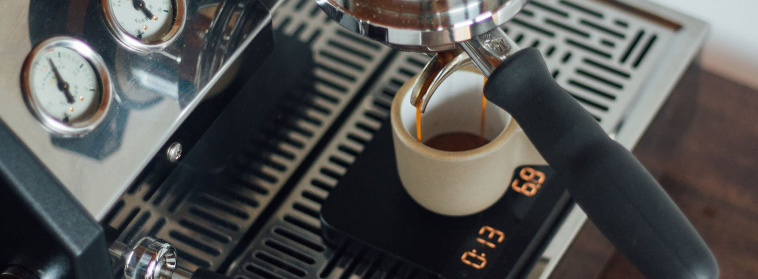 An espresso cup sitting on a coffee scale while brewed espresso pours from the portafilter above.