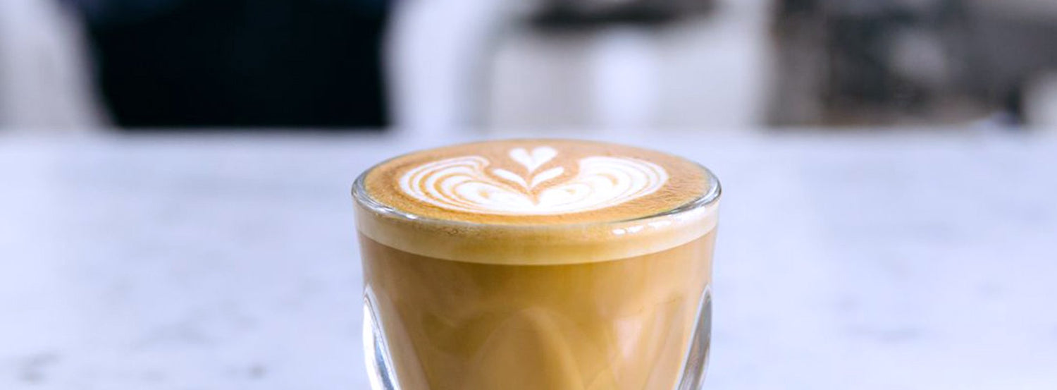 A small latte in a clear notNeutral glass, capped with latte art of a frond and hearts.