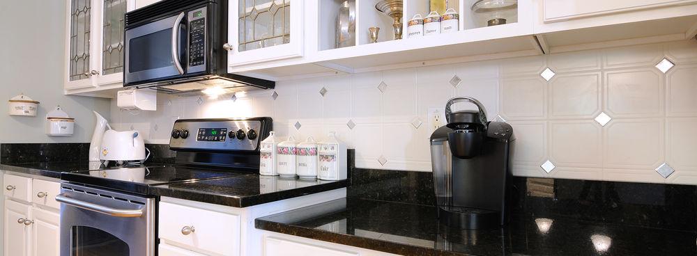 A white kitchen with black counters, lined with bags of coffee and a single-serve coffee maker.