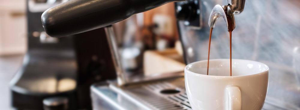 An espresso machine dispensing espresso through the spouts of a portafilter into a white coffee cup.