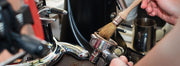 A person cleaning a portafilter with a brush at a coffee bar crowded with equipment