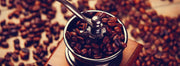 Coffee beans scattered around and inside of a manual coffee grinder
