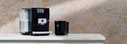 JURA Z10 Super Automatic Espresso Machine in black next to a black Cool Control on a counter in front of a neutral background.