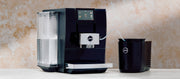 Close-up of a JURA Z10 Super Automatic Espresso Machine in black next to a black Cool Control on a counter in front of a neutral background.