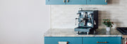 Black ECM Mechanika MAX Espresso machine on a kitchen counter with blue cabinets.