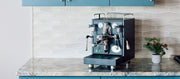 Close-up of a Black ECM Mechanika MAX Espresso machine on a kitchen counter with blue cabinets.