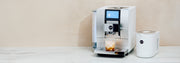JURA Z10 in Aluminum White next to a white cool control on a white counter top in front of a beige wall.