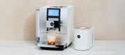 Close-up of the JURA Z10 in Aluminum White next to a white cool control on a white counter top in front of a beige wall.