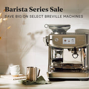 A Breville Barista Series espresso machine in brushed stainless steel, shown on a countertop with a milk frothing pitcher, stacked cups, and a green cloth against a tiled wall. Large sale text at the top reads 'Barista Series Sale' and 'SAVE BIG ON SELECT BREVILLE MACHINES'.