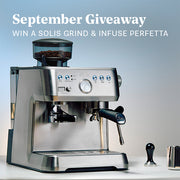 Solis Grind and Infuse Perfetta in Stainless Steel on a white counter top in front of a blue and white gradient background. Promotional text overlayed that reads "September Giveaway - Win a Solis Grind & Infuse Perfetta". 