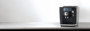 JURA J10 Twin in black on a gray and black counter top in front of a white wall.