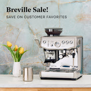 Breville Barista Express Impress next to yellow tulips on a white counter in front of a blue slate wall. Promotional text overlayed that reads "Breville Sale! Save on customer favorites".