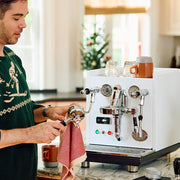 Person cleaning a portafilter in a holiday theme in front of a white ECM Synchronika.
